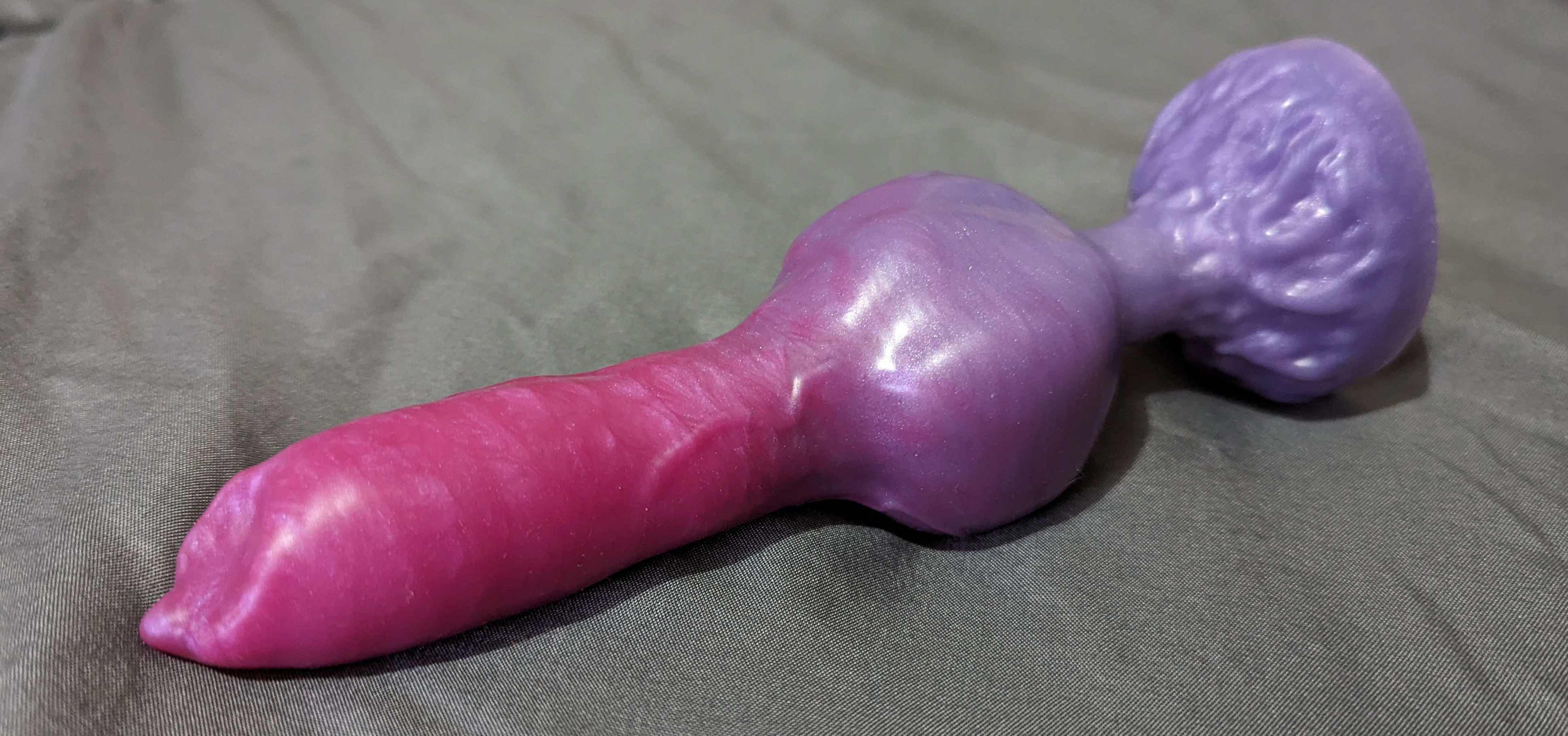 a photo of a purple and pink canine dildo on a grey bedsheet